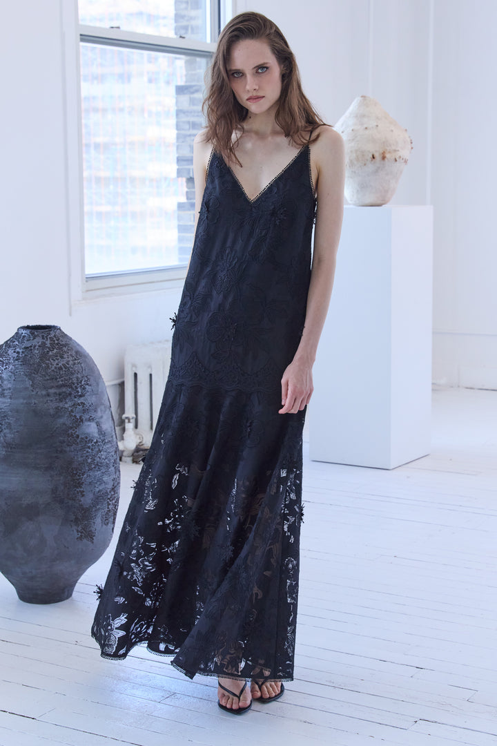 Woman wearing a black dress in a minimalistic room with large windows.