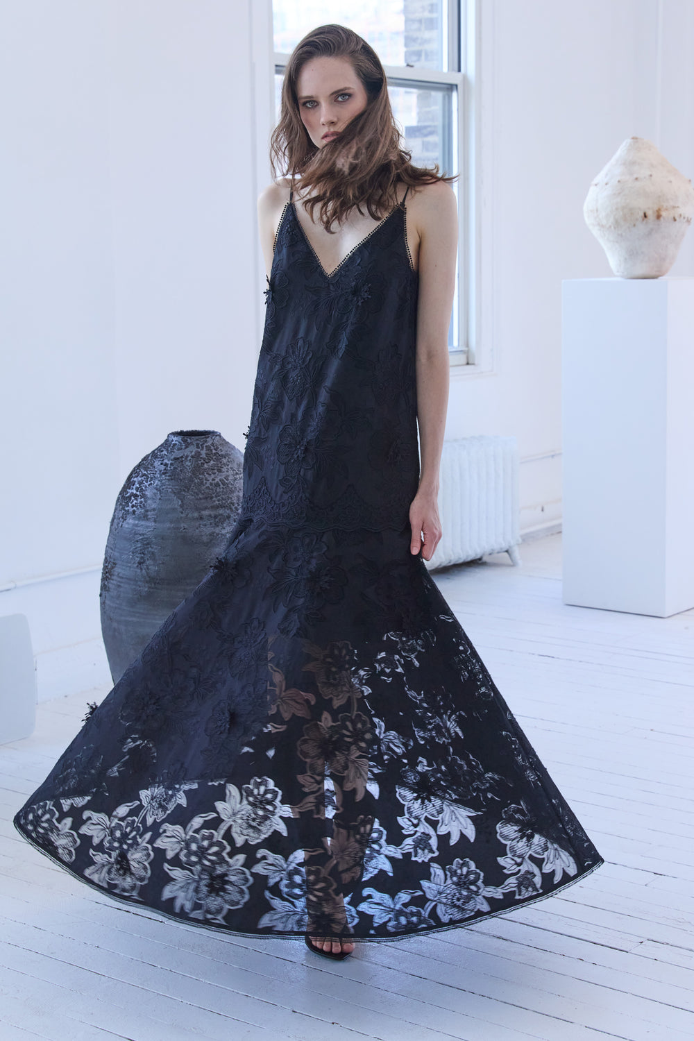 Woman wearing a black sleeveless dress with floral patterns in a minimalistic setting.