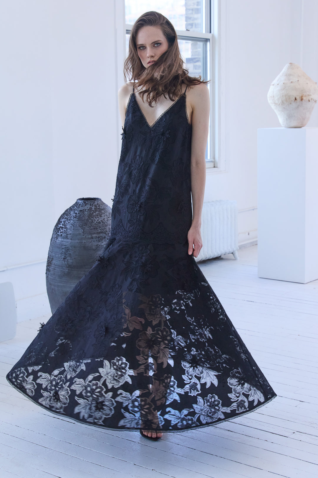 Woman wearing a black sleeveless dress with floral patterns in a minimalistic setting.