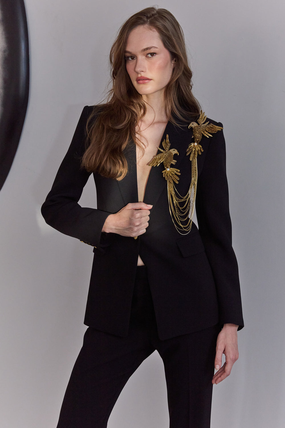 Model wearing a black suit with gold embroidery on a plain background