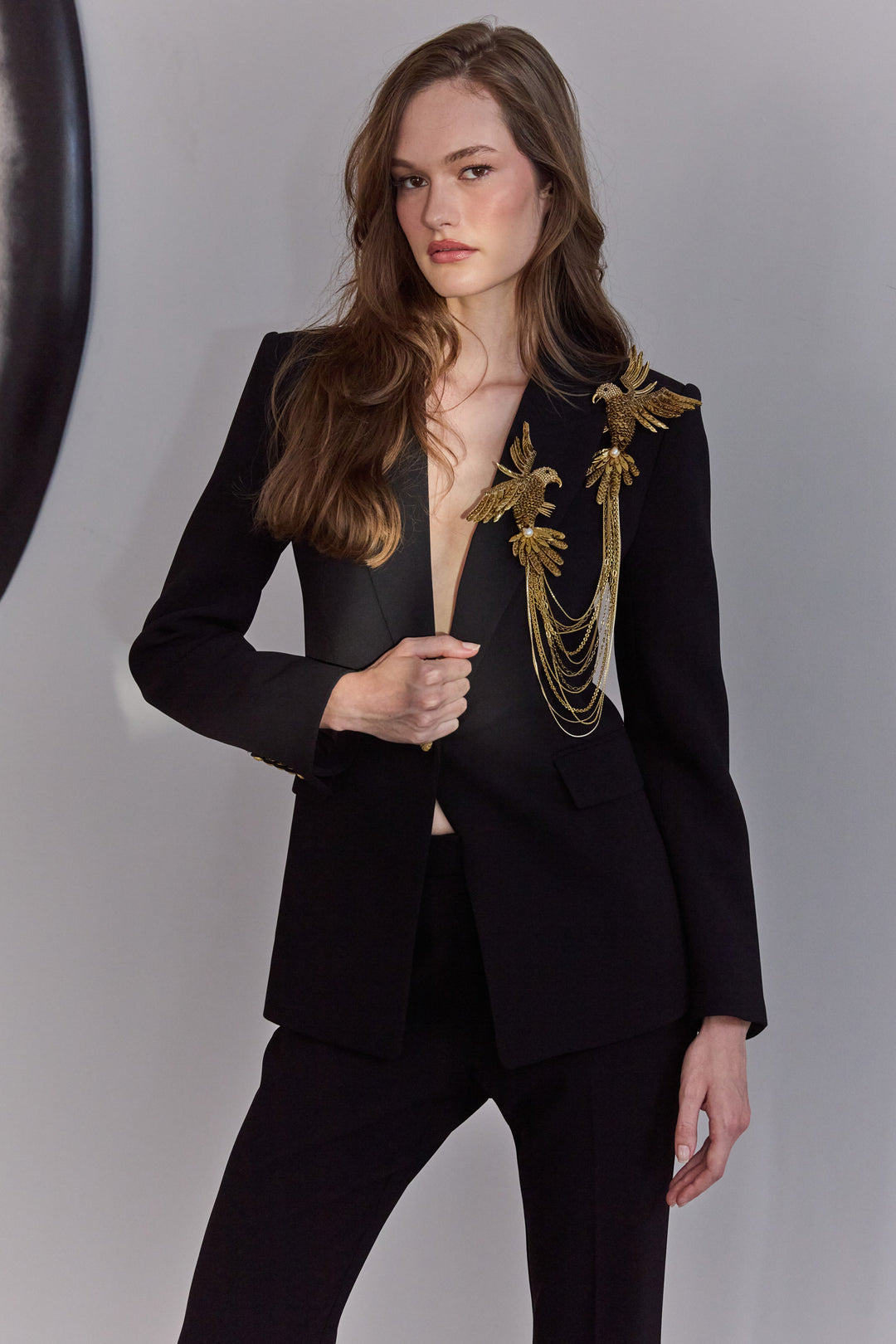 Model wearing a black suit with gold embroidery on a plain background