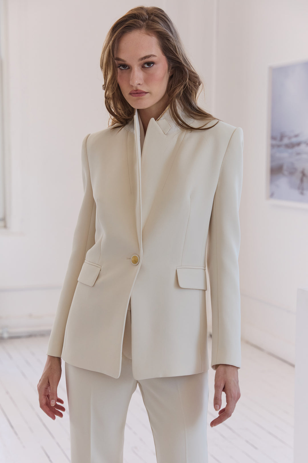 Woman wearing a cream-colored suit in a minimalistic room.