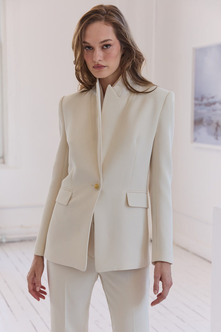 Woman wearing a cream-colored suit in a minimalistic room.