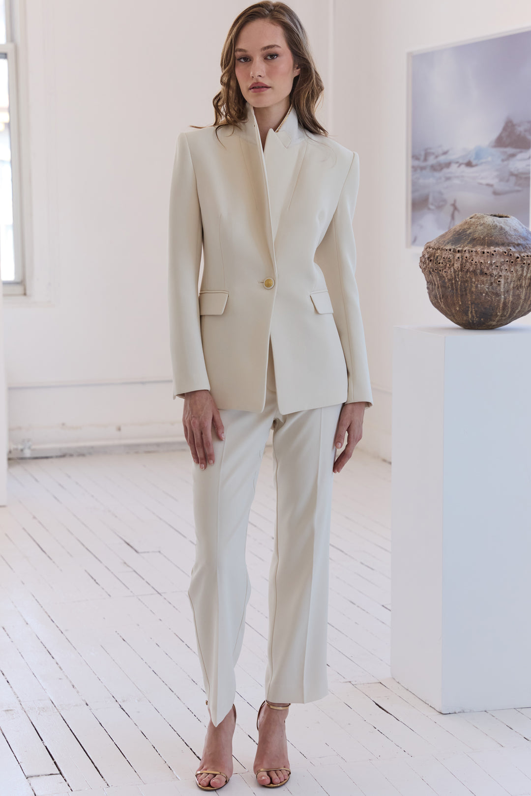 Woman wearing a beige suit in a minimalistic room with white walls and wooden floor.