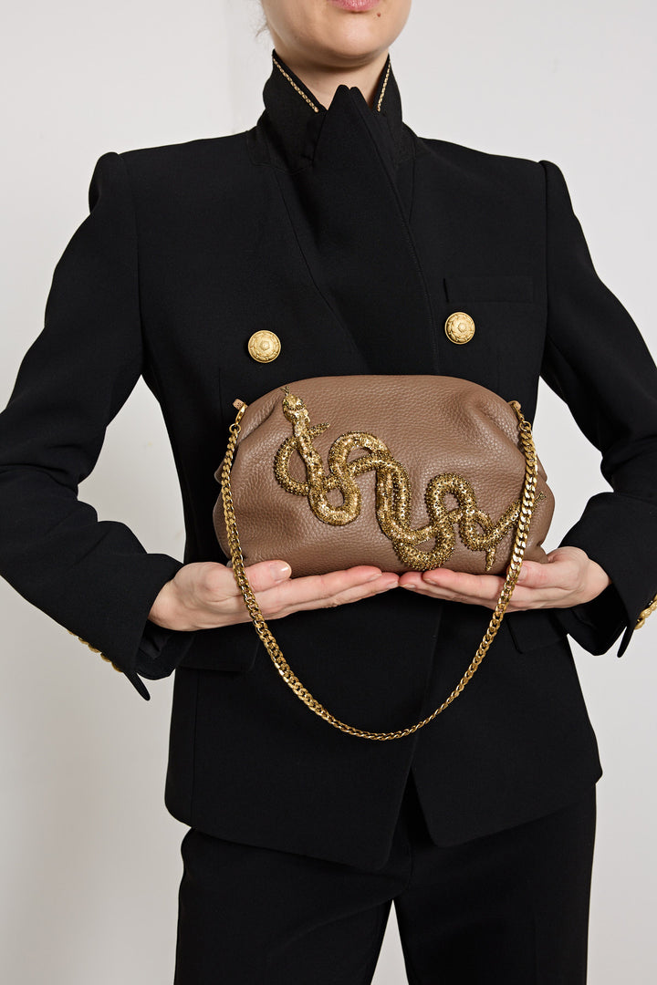 Person holding a brown clutch with gold chain and embellishments against a plain background