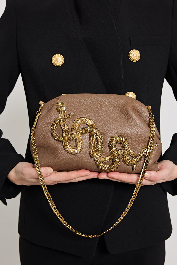 Brown handbag with gold chain and embellishments held by a person wearing a black coat.
