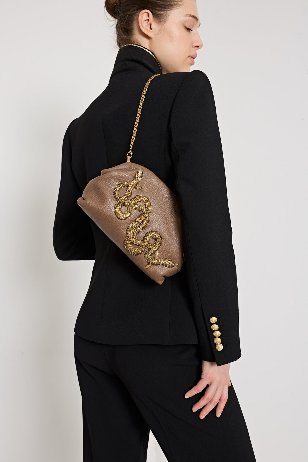 Woman in a black outfit holding a brown handbag with gold embellishments on a white background