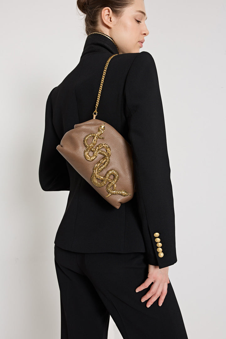 Woman in a black outfit holding a brown handbag with gold embellishments on a white background