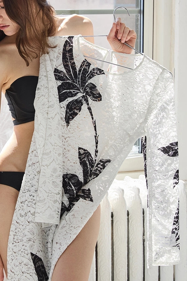 Woman holding a sheer white garment with black floral patterns in front of a window.